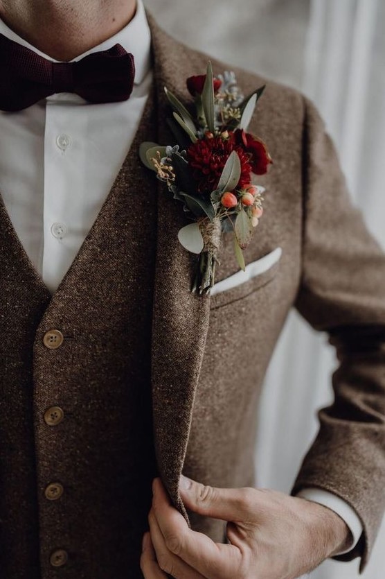 a brown tweed three-piece suit, a white button down, a burgundy velvet bow tie and a matching boutonniere