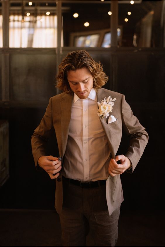 a modern groom's outfit with a brown pantsuit, a white shirt, a white dried flower boutonniere is very elegant