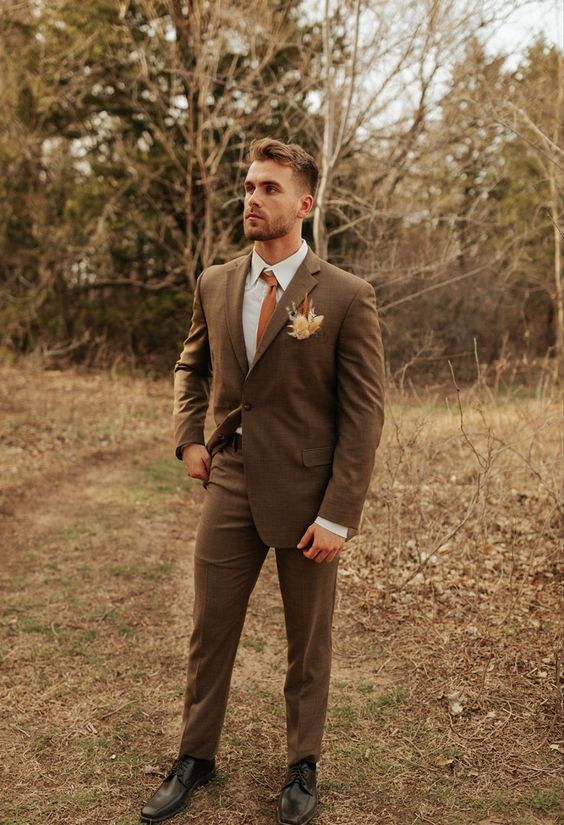 a refined fall groom's look with a brown checked pantsuit, a white shirt, an orange tie and a dried flower boutonniere