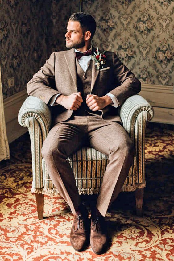 a sophisticated groom's look with a brown three-piece pantsuit, a white shirt, a burgundy bow tie, brown suede shoes and a boutonniere