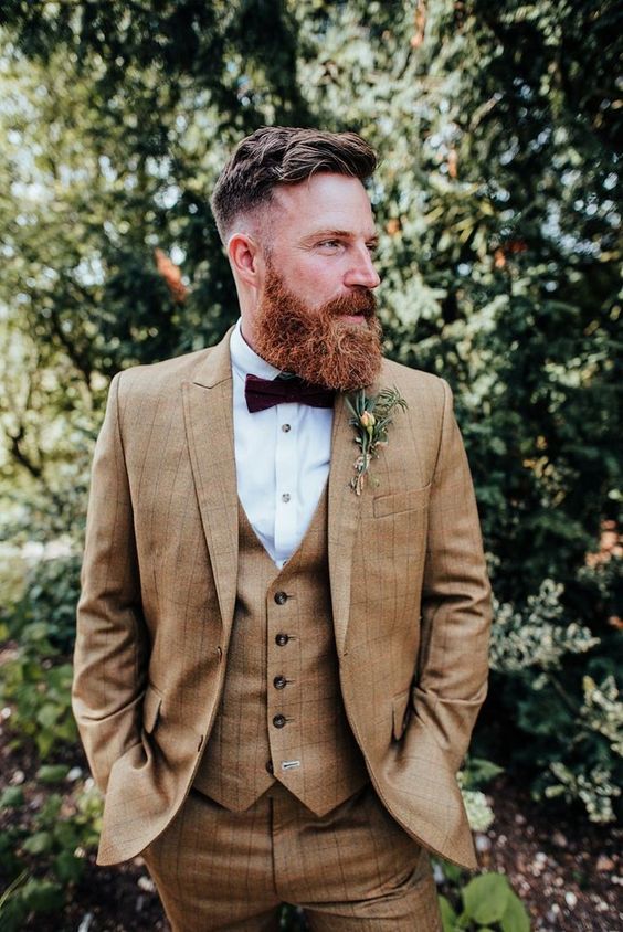 a vintage-inspired groom's look with a beige three-piece pantsuit, a white shirt, a burgundy bow tie and a boutonniere