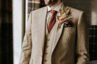 42 an elegant tan three-piece pantsuit, a white shirt, a rust-colored tie and a boutonniere with leaves