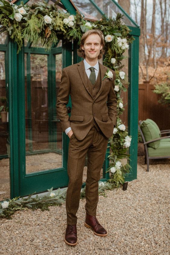 an elegant fall groom's look with a brown three-piece pantsuit, a white shirt, a green tie and brown boots