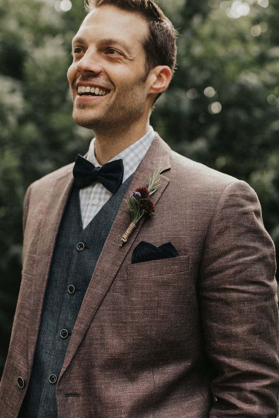 a boho groom's look with a checked shirt, a grey waistcoat, a brown blazer, a black bow tie and a handkerchief