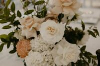 a beautiful and delicate wedding centerpiece of blush and white roses, white hydrangeas and a rust-colored chrysanthemum and greenery
