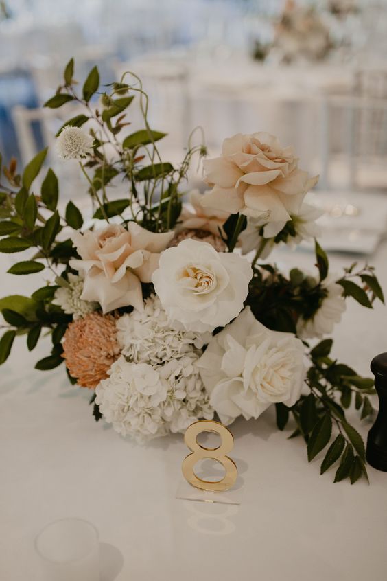 a beautiful and delicate wedding centerpiece of blush and white roses, white hydrangeas and a rust-colored chrysanthemum and greenery