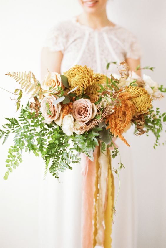 a bold fall wedding bouquet of blush roses, mustard chrysanthemums, greenery, fern, dried blooms and long ribbon is wow