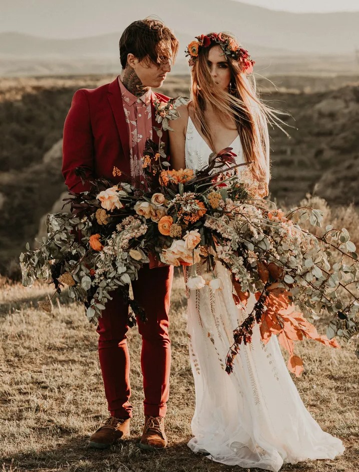 a bold groom's outfit with a deep red pantsuit, a pink printed shirt, amber shoes is a catchy idea for a boho wedding