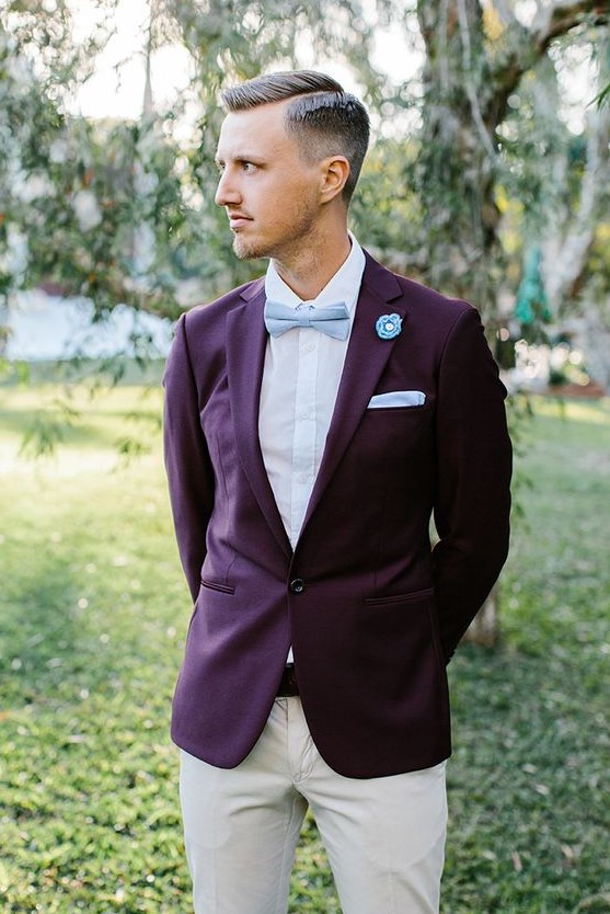 a bold groom's outfit with a purple blazer, a white shirt, a light blue bow tie and handkerchief, neutral pants