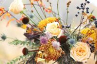 a bright autumn wedding centerpiece of yellow chrysanthemums, peachy roses, burgundy blooms, berries and greenery
