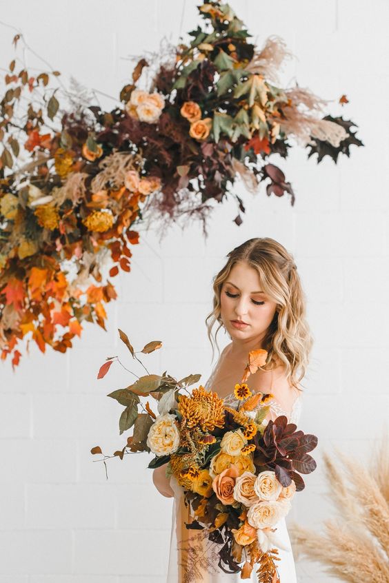 a bright autumnal wedding bouquet of yellow and neutral roses, mustard chrysanthemums, greenery and dark foliage is wow