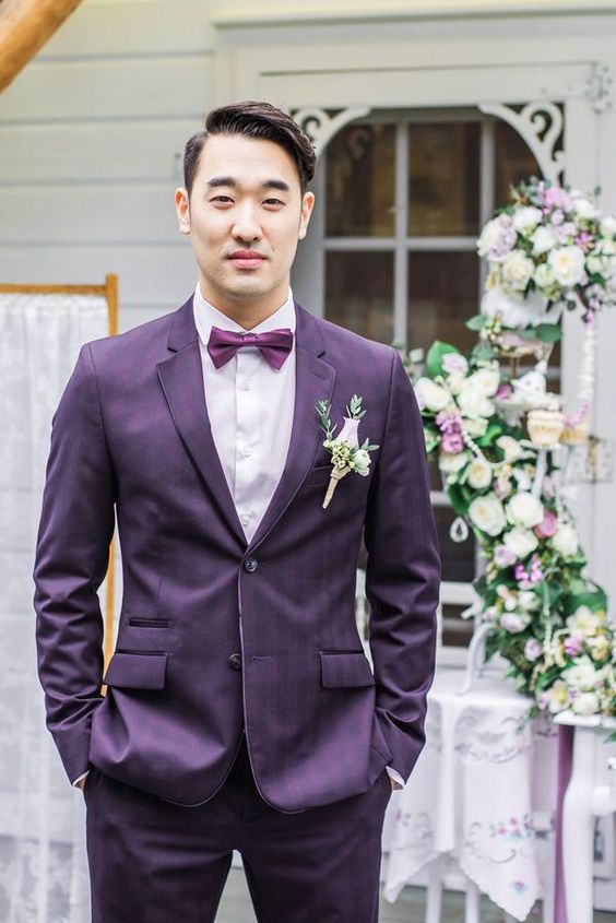 a bright groom's look with a purple plaid suit, a white shirt, a purple bow tie and a blush boutonniere