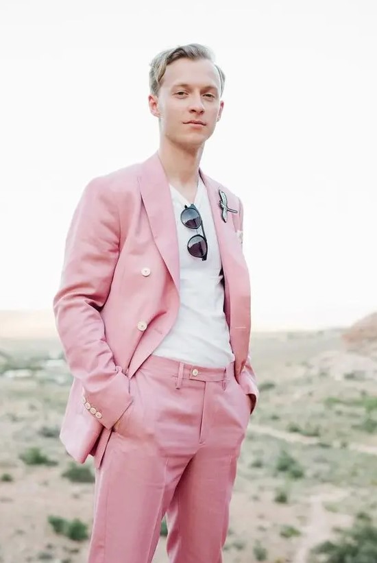 a bright pink groom's suit with a white t-shirt, sunglasses and a unique boutonniere for an offbeat wedding