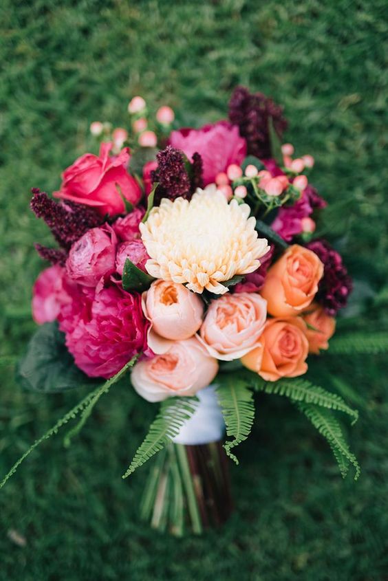 a bright wedding bouquet of hot pink roses, peonies, blush peony roses, berries, peachy mums and greenery is wow