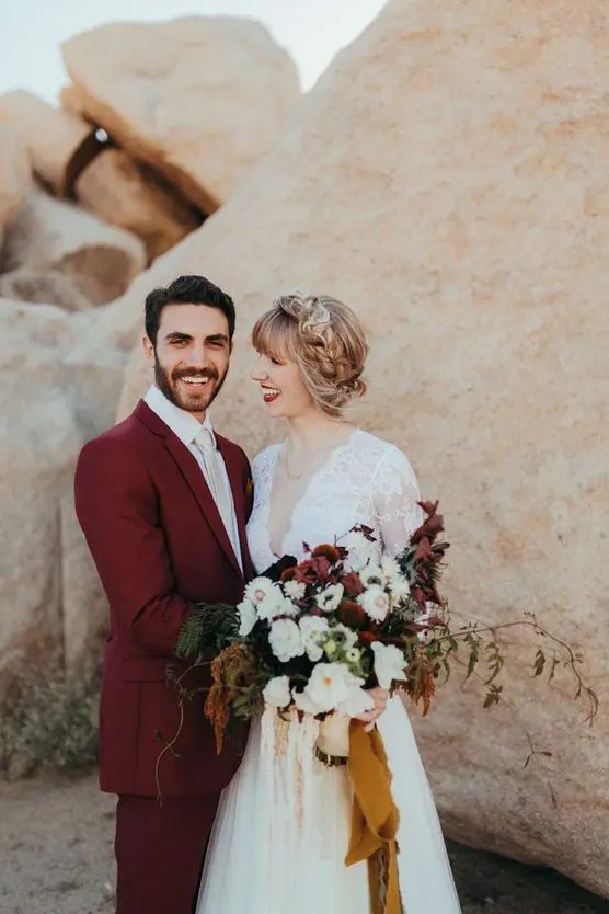 a bugundy suit, a white shirt and a white tie for a fantastic and bold groom's look in the desert