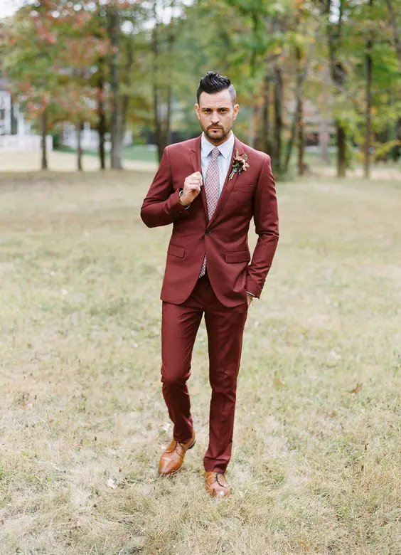 a burgundy pantsuit, a white shirt, a pink printed tie, amber shoes and a boutonniere plus a trendy haircut