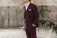 a burgundy three-piece pantsuit, a white shirt, a white bow tie and black velvet loafers for a refined fall groom’s look