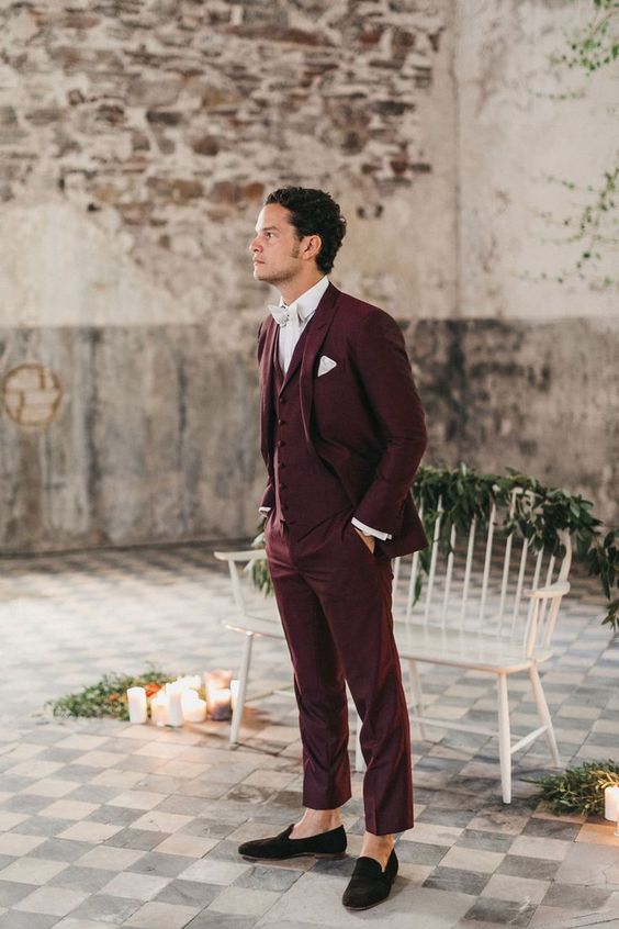 a burgundy three-piece pantsuit, a white shirt, a white bow tie and black velvet loafers for a refined fall groom's look