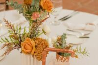 a catchy and bright fall wedding centerpiece of mustard roses, mums, deep purple blooms and greenery