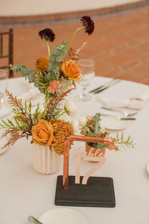 a catchy and bright fall wedding centerpiece of mustard roses, mums, deep purple blooms and greenery