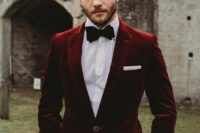 a catchy fall groom’s look with a white shirt, black trousers, a burgundy velvet blazer, a black bow tie