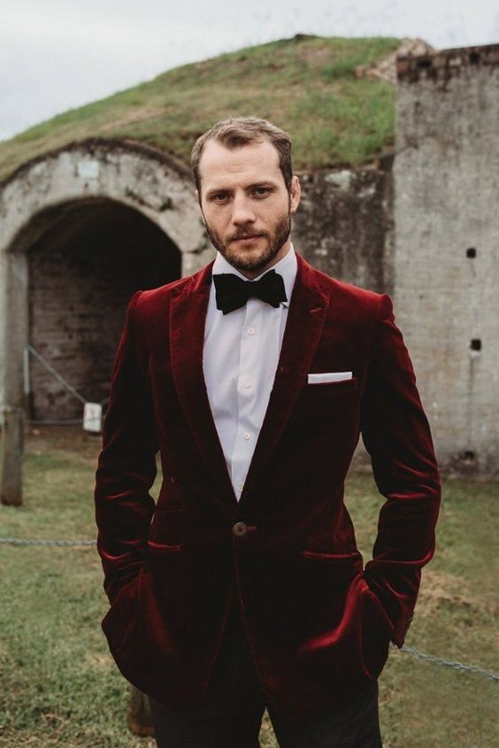 a catchy fall groom's look with a white shirt, black trousers, a burgundy velvet blazer, a black bow tie