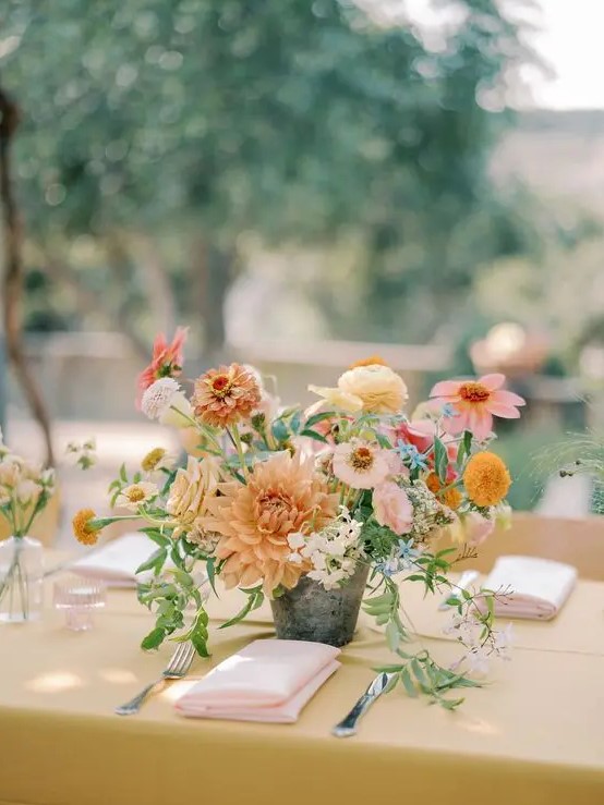 a catchy summer wedding centerpiece of yellow and pale rust dahlias, pink and neutral fillers and greenery