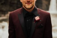 a chic and moody groom’s outfit with a black shirt, a burgundy blazer with black lapels and a bold boutonniere