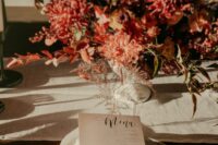 a chic fall wedding centerpiece of burgundy mums, greenery and some fall foliage is a gorgeous idea