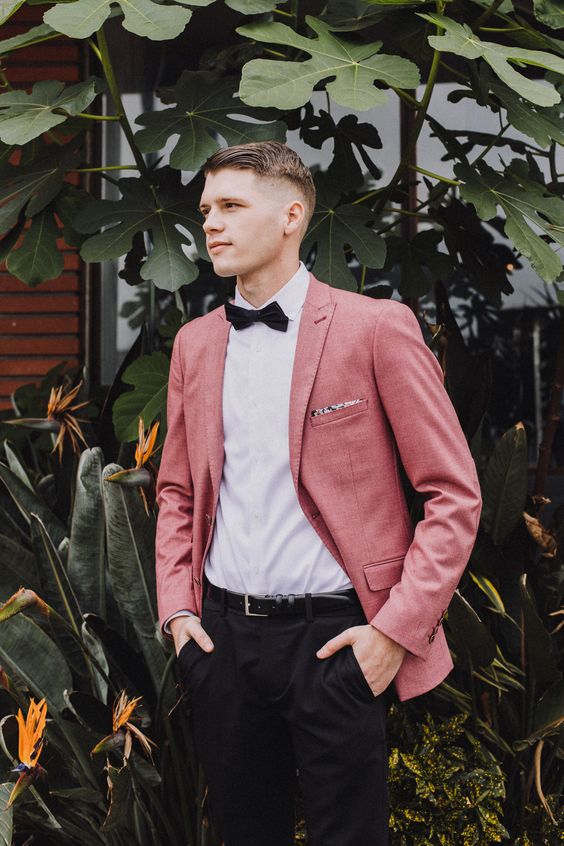 a chic groom's look with a white shirt, a pink blazer, a black bow tie and black pants is a cool idea for a modern wedding