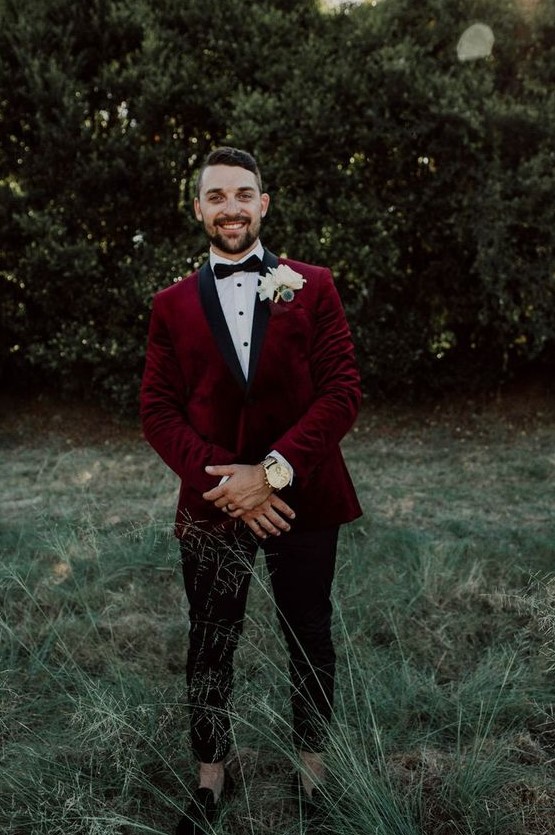 a chic groom's outfit with a burgundy velvet blazer with black lapels, a black bow tie, black cropped pants and moccasins