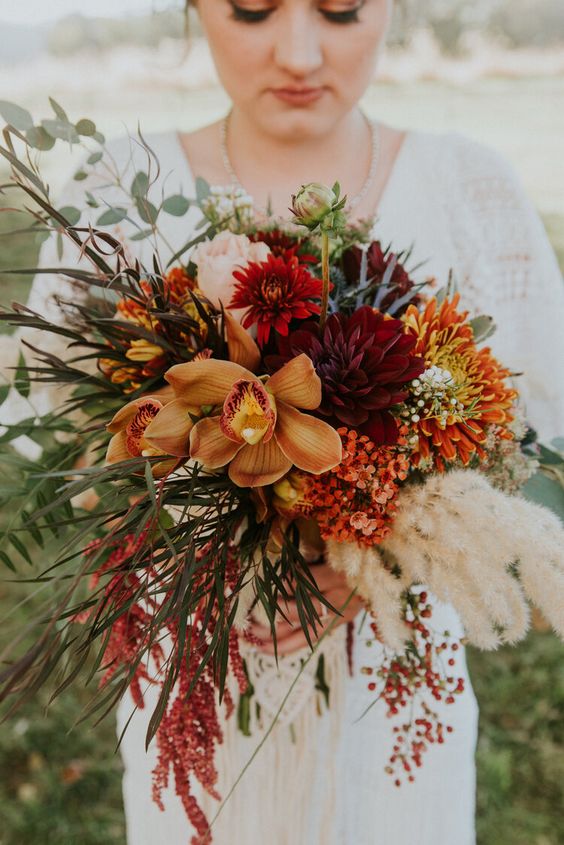 a colorful fall wedding bouquet of burgundy and red dahlias, rust orchids, some small yet bright fillers, chrysanthemums and greenery plus amaranthus