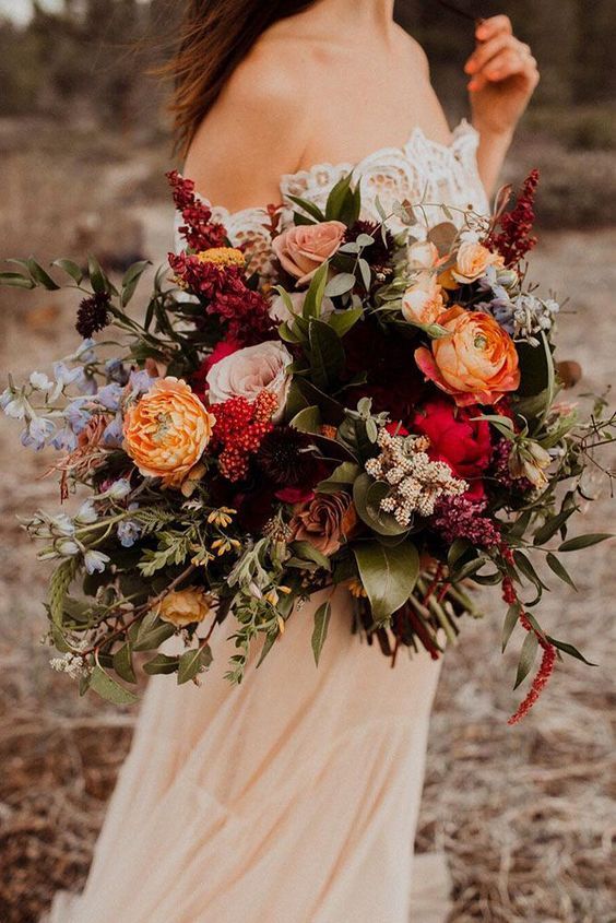 a colorful fall wedding bouquet of orange ranunculus, chrysanthemums, pink roses, greenery and amaranthus