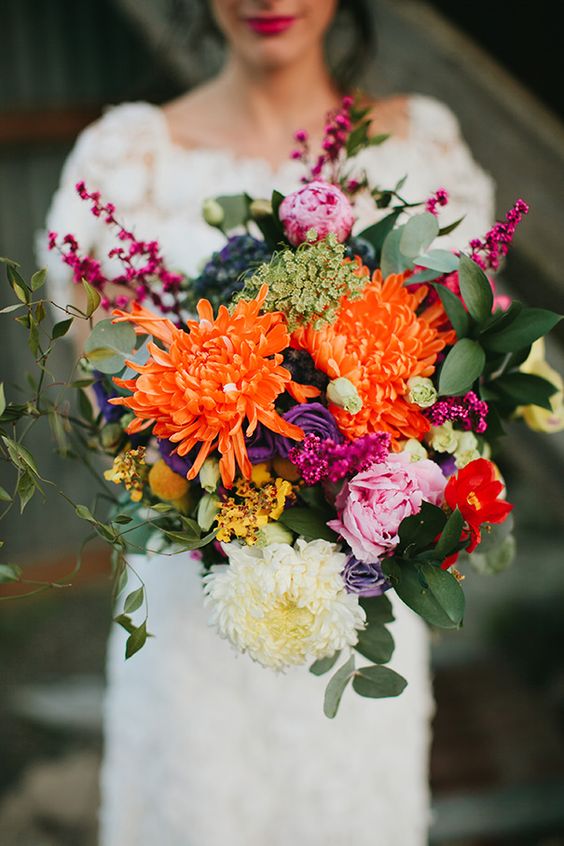 a colorful fall wedding bouquet of white and orange chrysanthemums, pink peonies and purple ranunculus and greenery