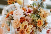 a colorful fall wedding centerpiece of yellow and blush roses, mums, carnations, greenery and grasses is cool