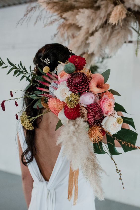 a colorful tropical wedding bouquet of white, pink roses, callas, king proteas, seed pods, tropical fronds and pampas grass