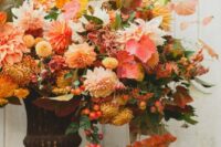 a dreamy fall wedding centerpiece in a vintage urn, with pink and peachy dahlias, yellow mums, bold fall leaves and berries