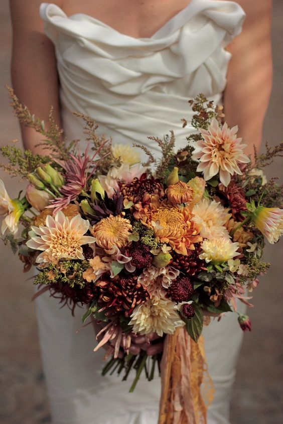 a fall wedding bouquet of blush, rust and burgundy dahlias, chrysanthemums, greenery and herbs, some ribbons
