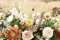 a fall wedding centerpiece of light pink roses, orange mums, other blooms in neutral shades and greenery