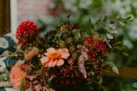a fall wedding centerpiece of pink and burgundy blooms including dahlias and mums, some berries and greenery