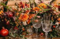 a jaw-dropping fall wedding centerpiece of orange, yellow and burgundy blooms, greenery, berries and fruit is amazing
