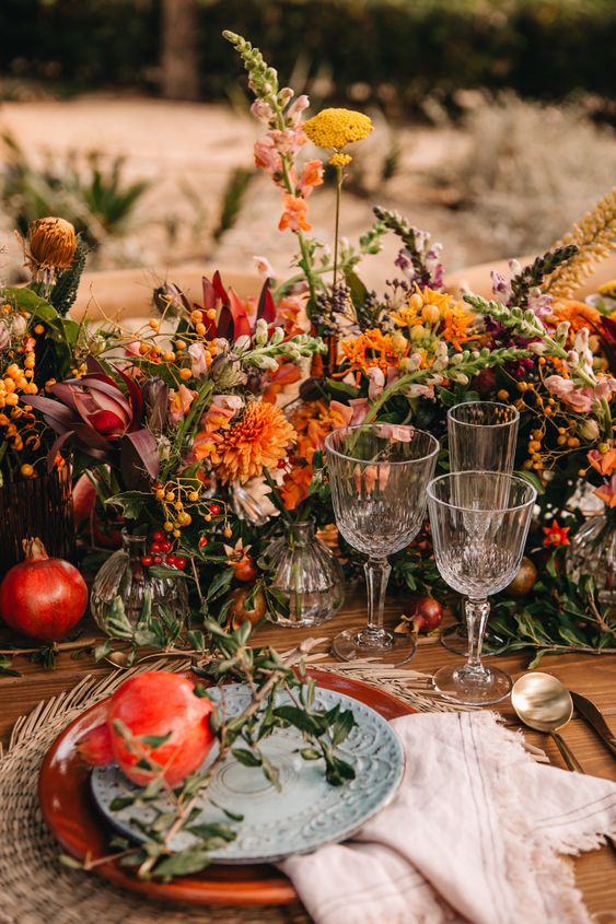 a jaw-dropping fall wedding centerpiece of orange, yellow and burgundy blooms, greenery, berries and fruit is amazing