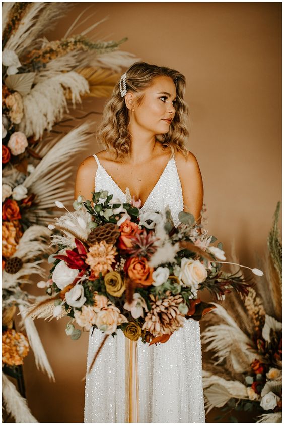 a lovely glam fall wedding bouquet of white, blush and orange roses, lotus slices, greenery, chrysanthemums, grasses is amazing