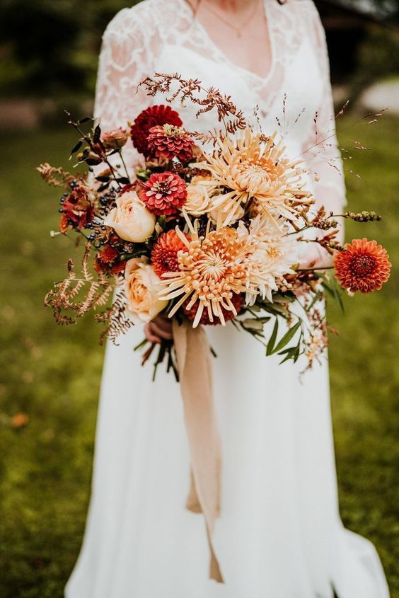 a lush fall wedding bouquet of red dahlias, blush and peachy roses, rust chrysanthemums, greenery and privet berries
