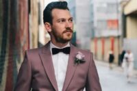a mauve groom’s suit with a white shirt and a burgundy velvet bow tie for a unique feel