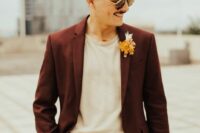 a modern and relaxed groom’s look with a burgundy pantsuit, a neutral t-shirt, a brown belt and a bold boutonniere