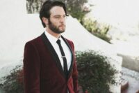a modern and stylish groom’s look with a burgundy velvet blazer with black lapels and a black tie, black trousers