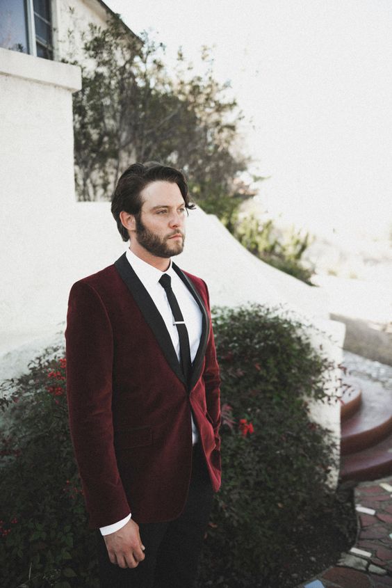 a modern and stylish groom's look with a burgundy velvet blazer with black lapels and a black tie, black trousers