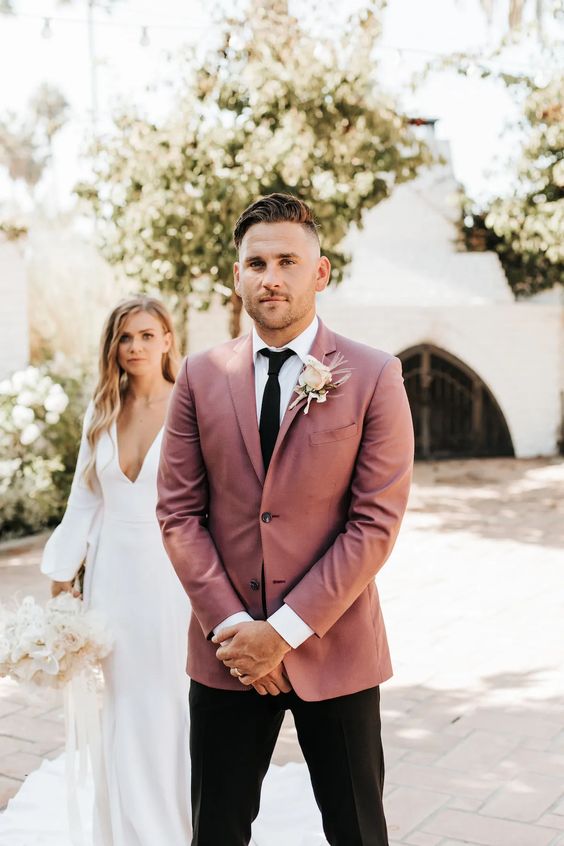 a modern groom's outfit with a white shirt, a mauve blazer, a black tie and pants, a blush rose boutonniere