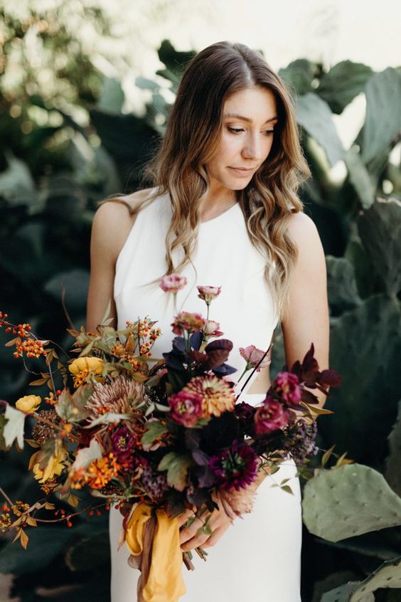 a moody autumnal wedding bouquet of marigolds, pink and rust blooms, greenery and dark foliage and berries